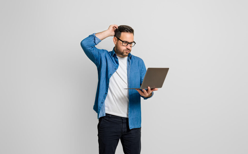 Man standing up holding his laptop and is confused by Outlook Ribbon having extra space and missing commands in Touch/Mouse Mode